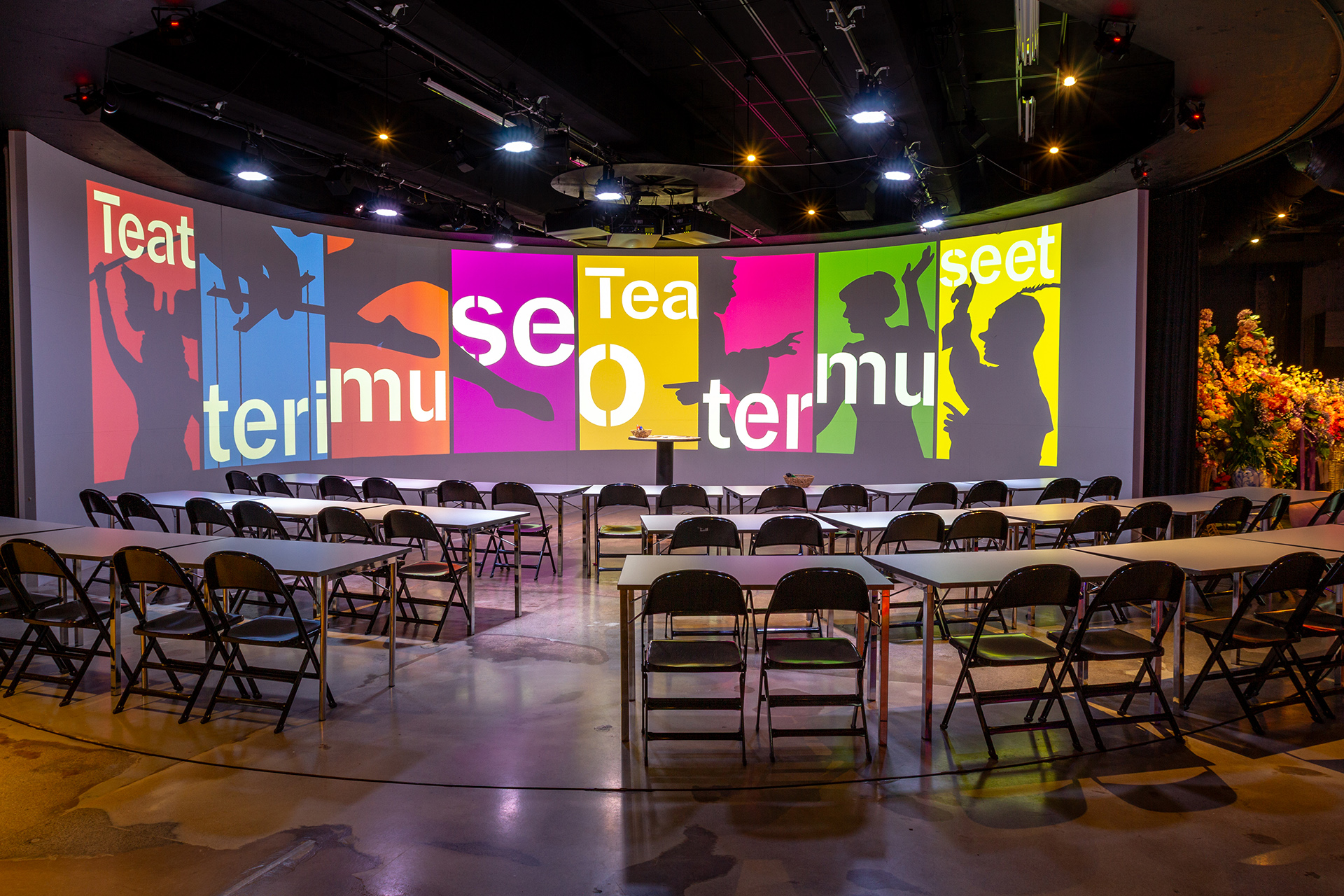 Seminaarijärjestely maneesissa, pöydät ja tuolit kaarevissa riveissä.