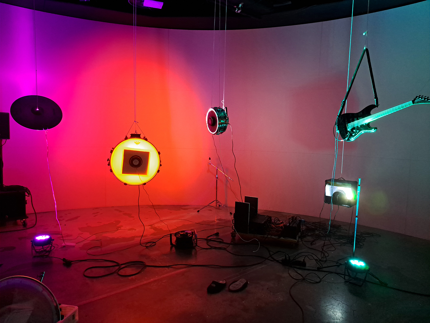 Musikinstrument upplysta med olikfärgade lampor hänger från taket, inklusive en cymbal, en bastrumma, en mindre trumma och en elgitarr.