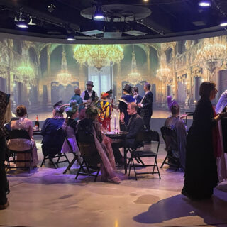 Ihmisiä juhlimassa Maneesissa, pienet pöytäryhmät.